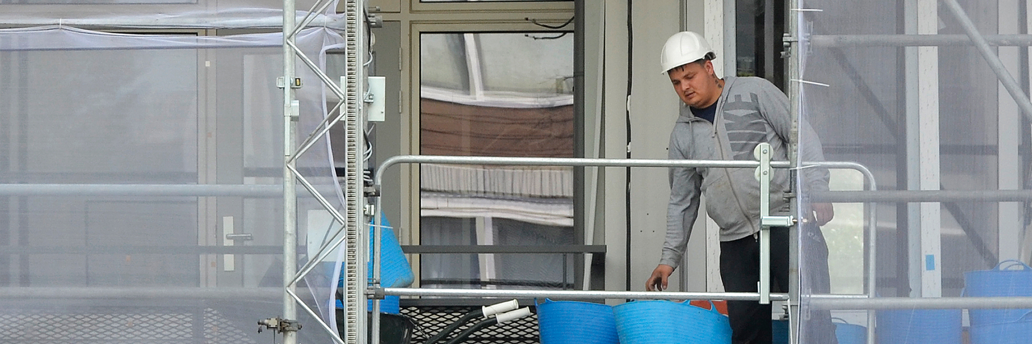 Bouwvakker die een woning aan het verbouwen is en die op een stijger staat met een witte helm