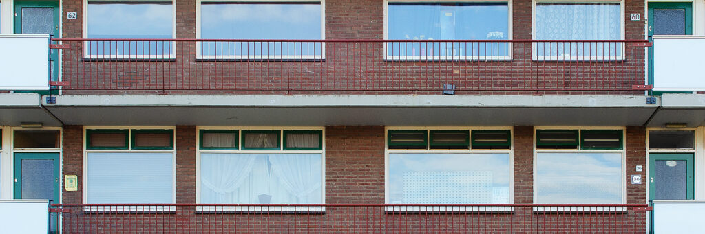 Appartementencomplex met bruine bakstenen en bordeaux rode balkon balustrades met groene deuren