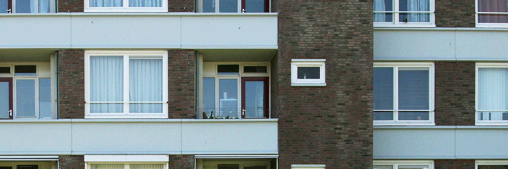 Appartementencomplex met bruine bakstenen muur en witte kozijnen met rode deuren