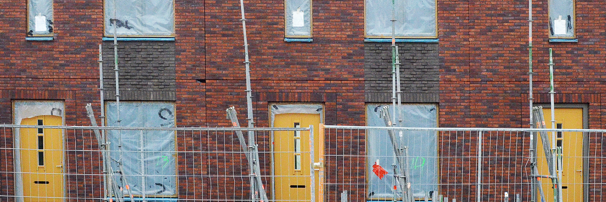 Eengezinswoningen die worden verbouwd met zeil voor de ramen, bruine bakstenen muur en gele deuren met een hek ervoor