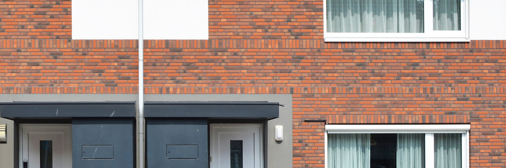Eengezinswoning met rode bakstenen muur, grijze deur en witte kozijnen