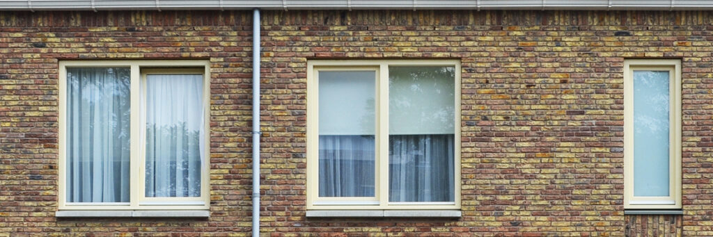 Donker en lichtbruine bakstenen muur met crème kozijnen