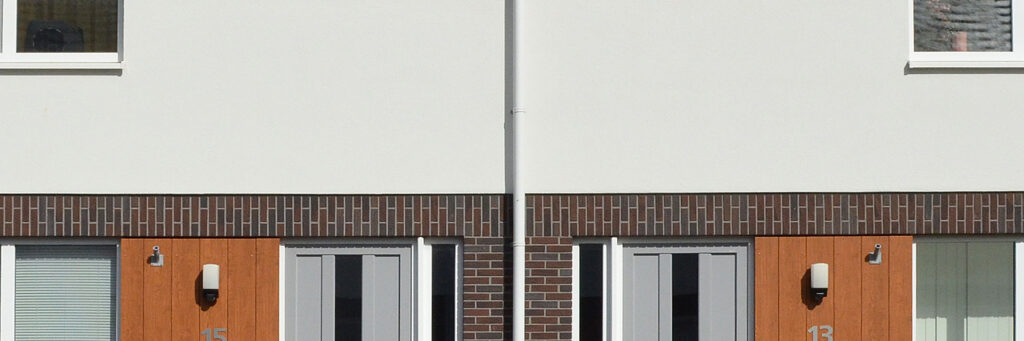 Eengezinswoningen met bruine bakstenen muur met een witte bovenverdieping muur en grijze deuren met houten panelen ernaast