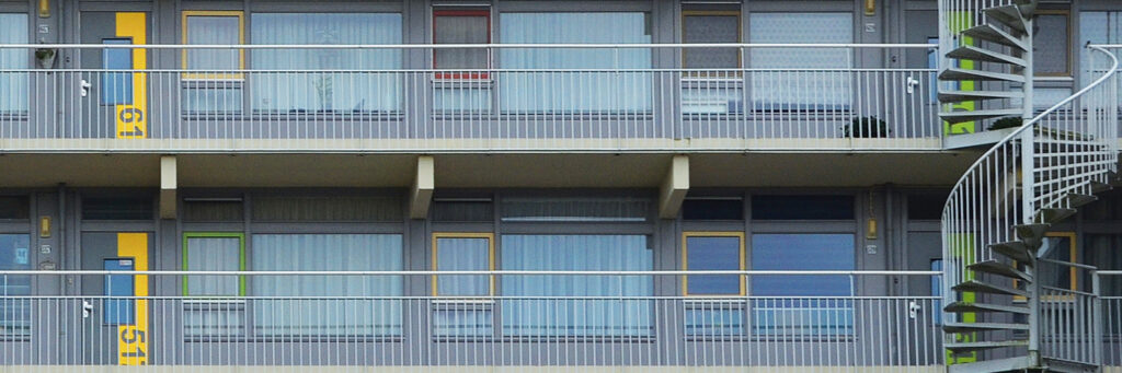 Appartementencomplex met een grijze balustrade en grijze kozijnen en verschillende kleuren deuren