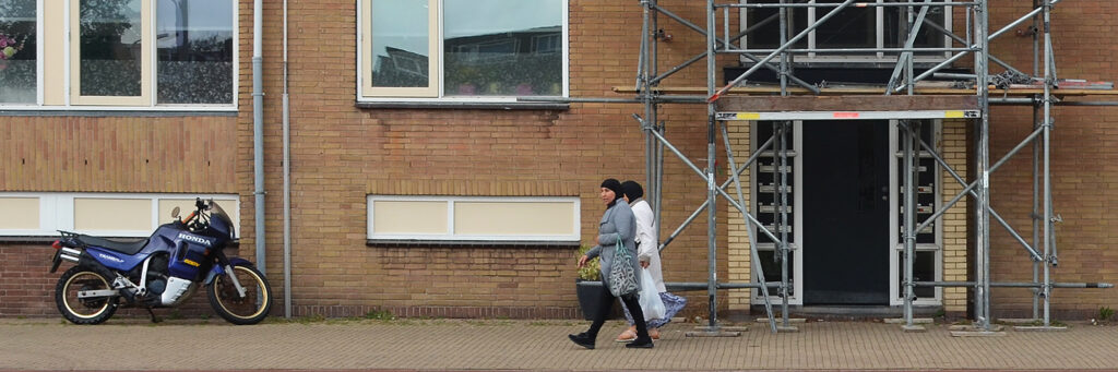 Woning met witte kozijnen en een stijger voor de deur met twee voorbij lopende mensen