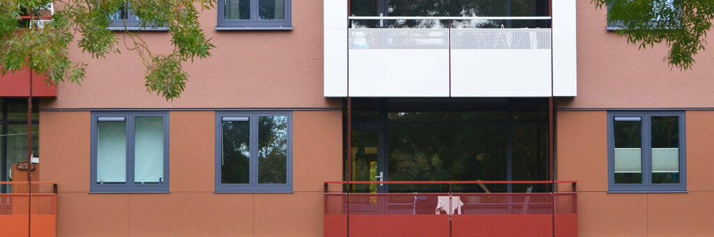 Appartementencomplex met bruine bakstenen muur met blauwe kozijnen en een witte en een rode balkon