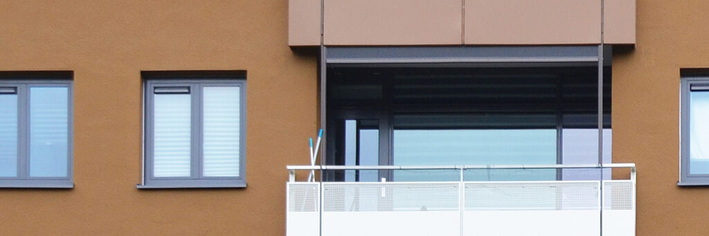 Appartementencomplex met een bruine bakstenen muur met grijze kozijnen, en een wit balkon