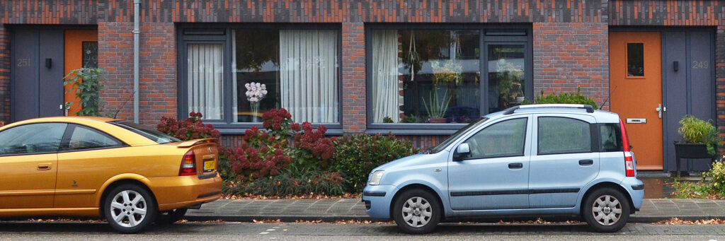 Woningen met oranje deuren met daarvoor een gele en een blauwe auto