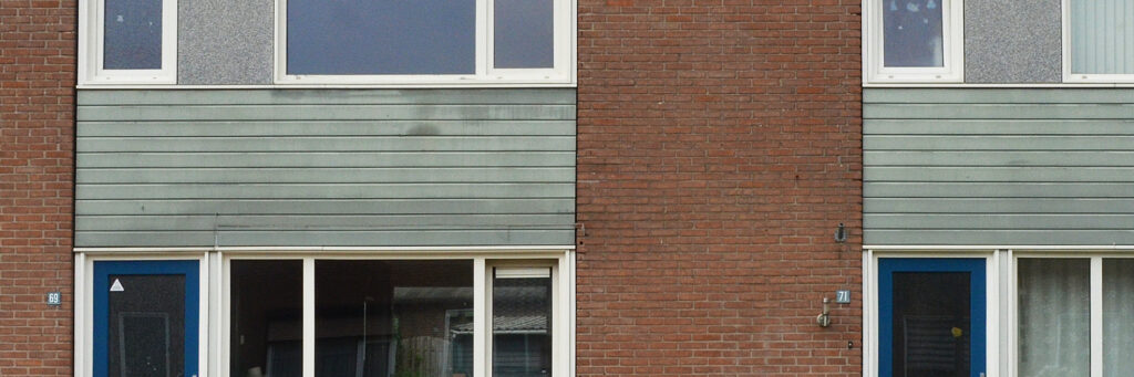 Woningen met bruine bakstenen muur, witte kozijnen en groene houten planken