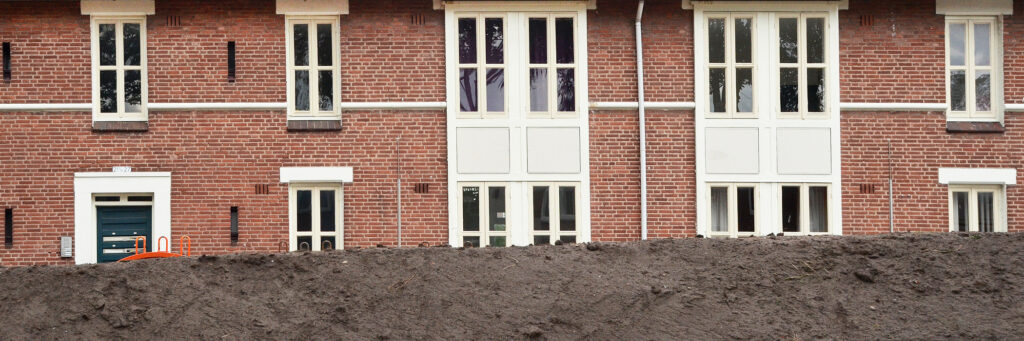 Woningen met bruine bakstenen gevel, witte kozijnen en grote stapel zand voor de deur