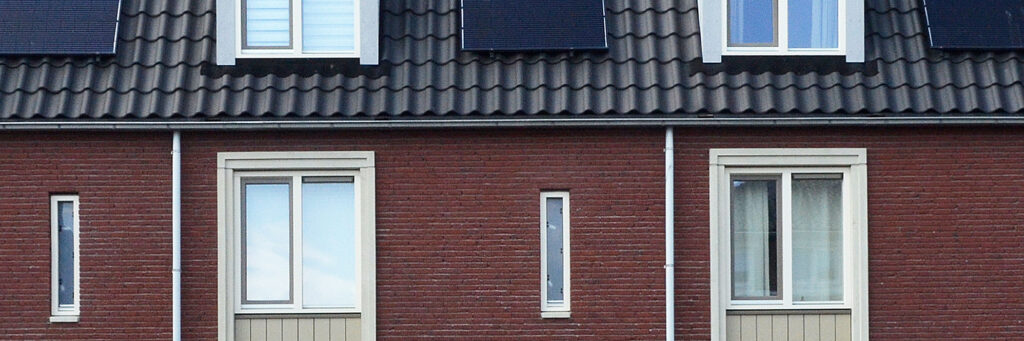 Woning met donkerrode bakstenen muur, witte kozijnen en zonnepanelen op zwarte dakpannen