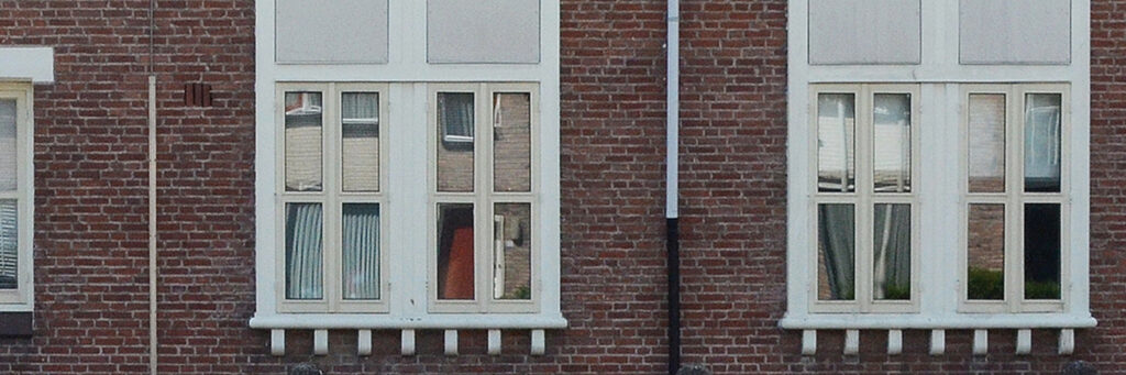 Woning met bakstenen muur, regenpijp en witte kozijnen