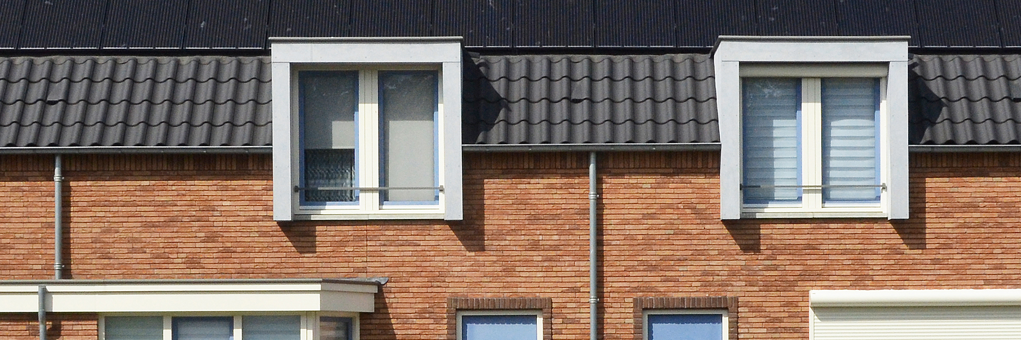 Woning bovenverdieping met een bruine bakstenen muur, witte kozijnen, zwart dak met zonnepanelen
