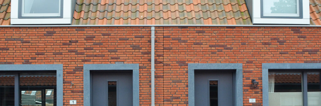 Woningen met diverse kleuren bakstenen muur, diverse kleuren dakpannen en grijze kozijnen en deuren