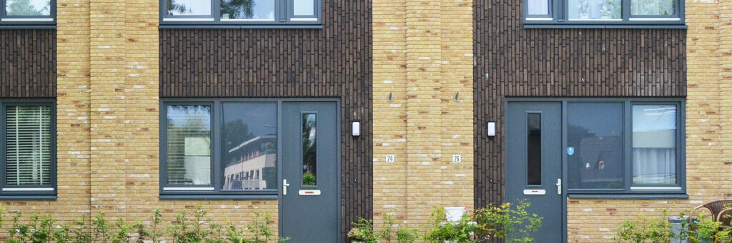 Woningen met crème bakstenen muur met stukje bruine gevel en grijze kozijnen en deuren