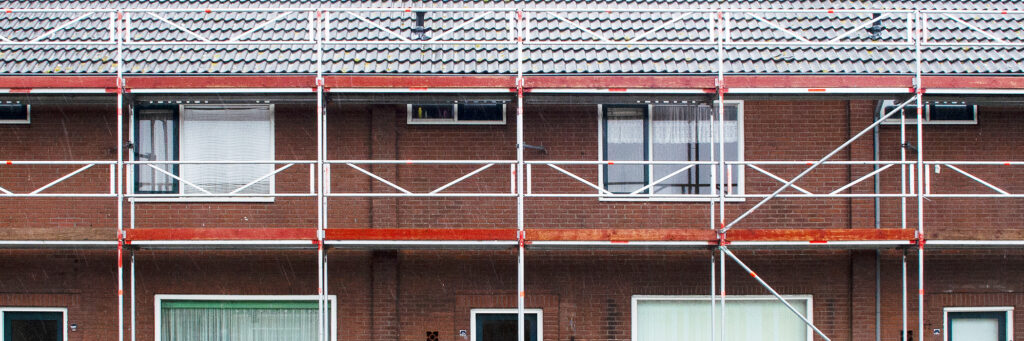 Bruine huizen met grijs dak en bouwsteigers ervoor