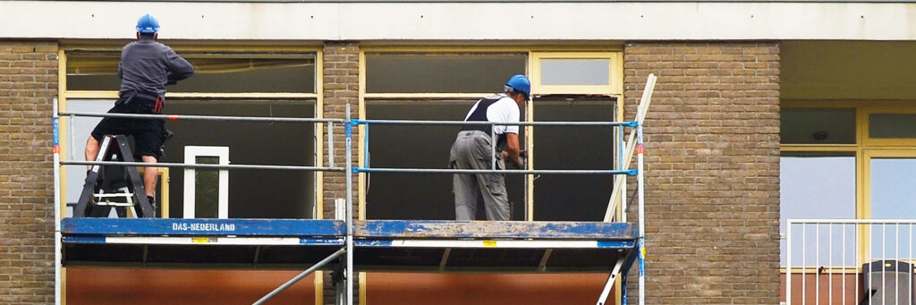 Appartementencomplex met een stijger ervoor met twee bouwvakkers erop die werken