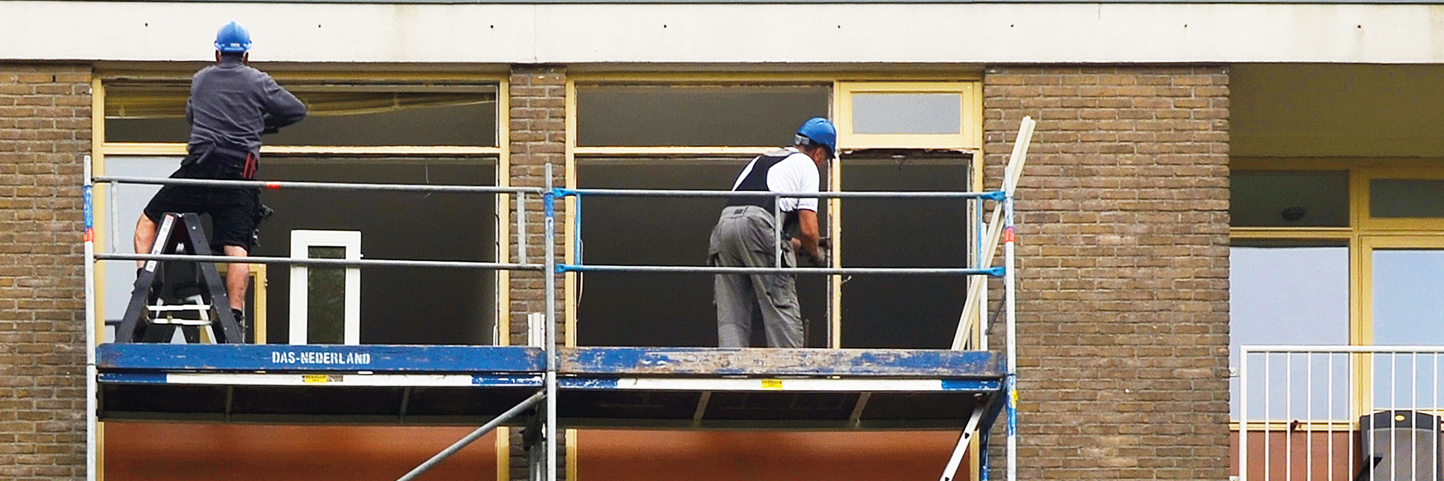 Appartementencomplex met een stijger ervoor met twee bouwvakkers erop die werken