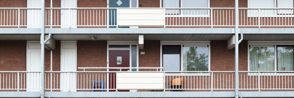 Appartementencomplex met een bruine bakstenen gevel, bruine deuren, witte kozijnen en witte balustrade