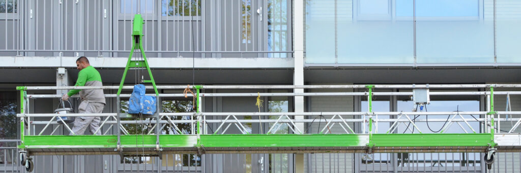 Apparteementencomplex met een groene kraanbak ervoor met een bouwvakker