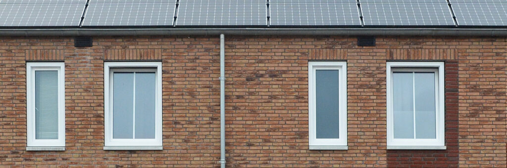 Woning bovenste verdieping met bruine bakstenen gevel, witte kozijnen, zonnepanelen en een regenpijp
