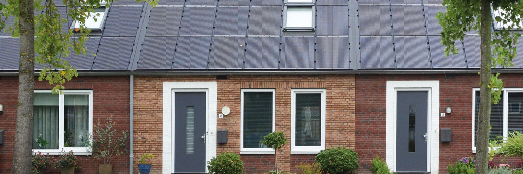 Woning met bruine bakstenen muur, witte kozijnen, donkergrijze deuren, zonnepanelen en bomen voor de deur