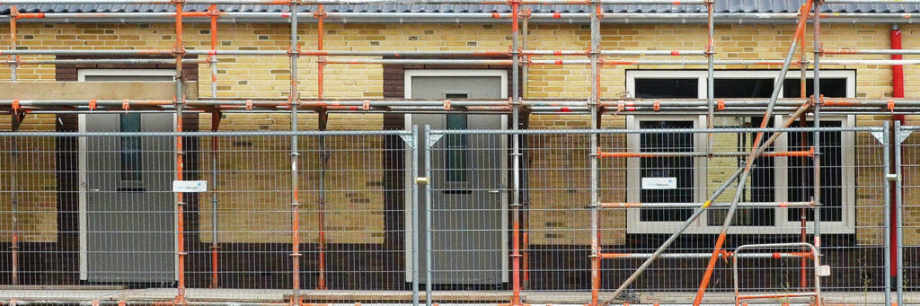 Woning met houten platen in de gevel, witte kozijnen met grijze deuren, stijgers en een hek voor de woningen