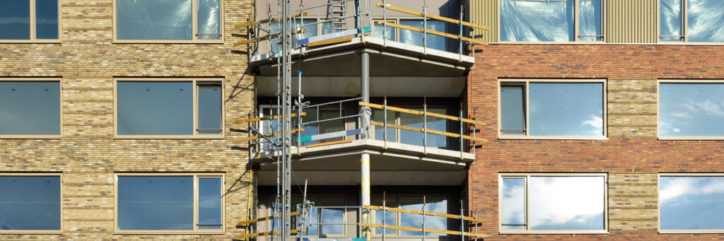 Appartmentencomplex dat wordt verbouwd met driehoekige balkons en bruine bakstenen gevel