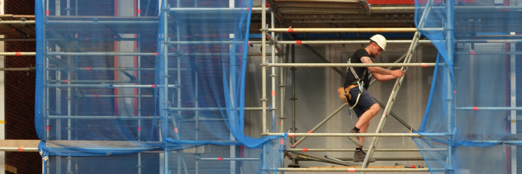 Appartementencomplex die in de stijgers staat met blauwe doeken en een bouwvakker