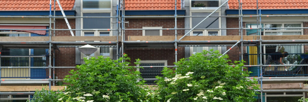 Appartementencomplex met donkerbruine bakstenen geven met rode dakpannen, stijgers voor het complex en bomen