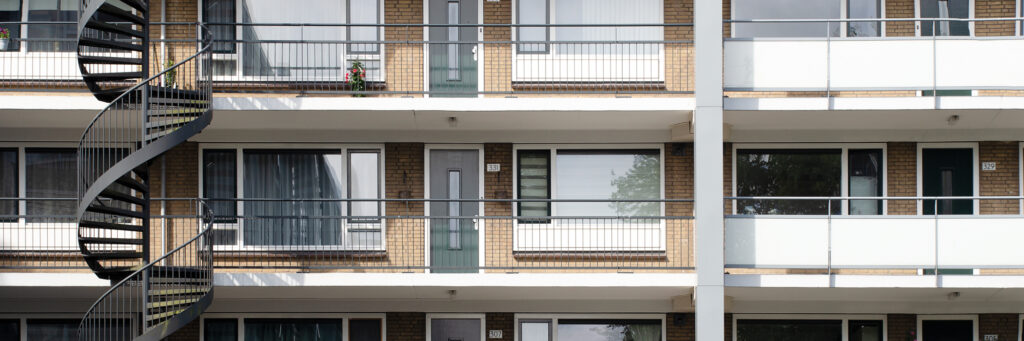 Appartementencomplex met lichtbruine bakstenen gevel, witte kozijnen, grijze deuren en een wenteltrap