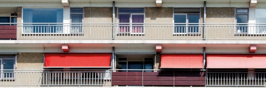 Appartementencomplex met crème gevel, witte kozijnen en rode zonwering