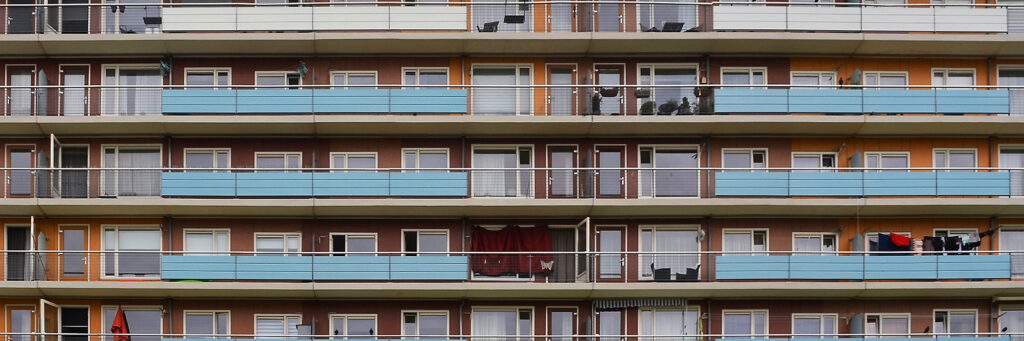 Appartementencomplex met bruine bakstenen gevel, witte kozijnen met witte balustrade met blauwe platen ervoor