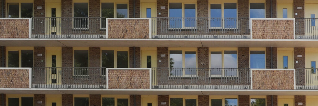 Appartementencomplex met bruine bakstenen muur, gele kozijnen en grijze balustrade
