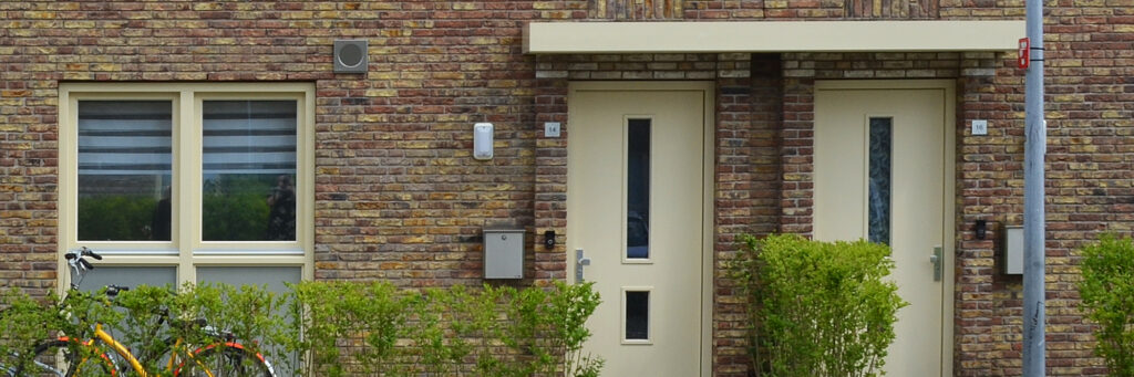 Woningen met bruine bakstenen gevel, crème kozijnen en deuren met een hegje ervoor
