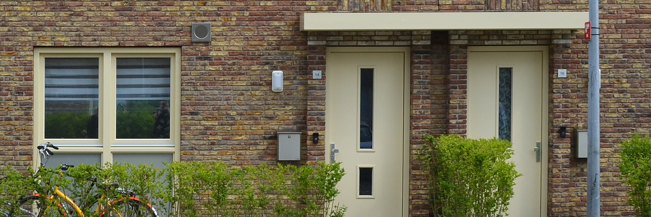 Woningen met bruine bakstenen gevel, crème kozijnen en deuren met een hegje ervoor