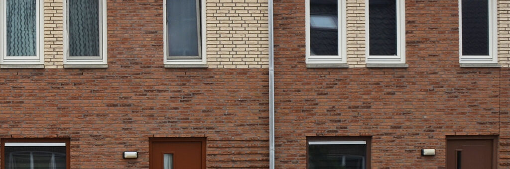 Woningen met donkerbruine bakstenen gevel, witte kozijnen en rode deur met regenpijp