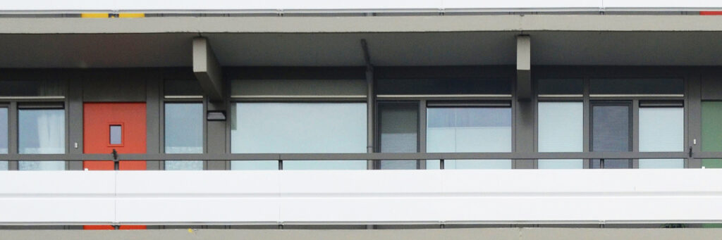 Appartementencomplex met grijze gevel, grijze kozijnen, oranje deur en witte balustrade
