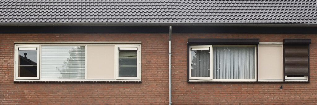 Woningen met bruine bakstenen gevel, crème kozijnen en zwarte dakpannen met een regenpijp