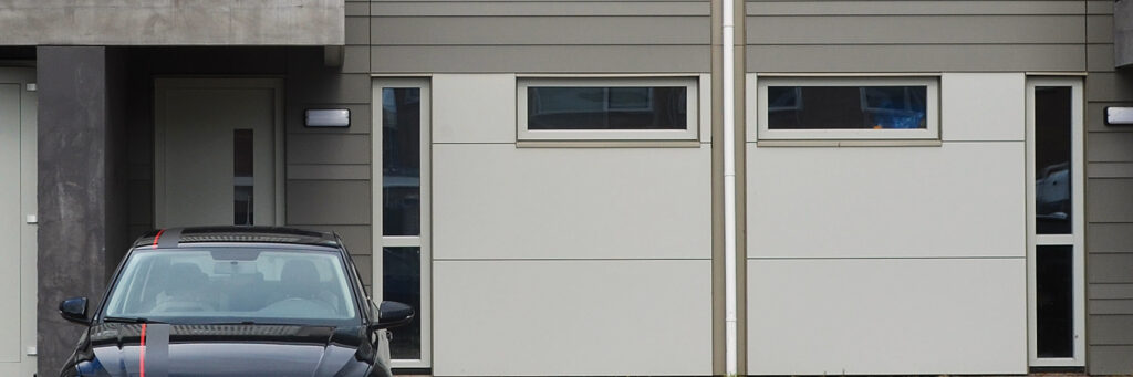 Woning met grijze platen gevel, met witte platen, witte kozijnen en een zwarte auto voor de deur
