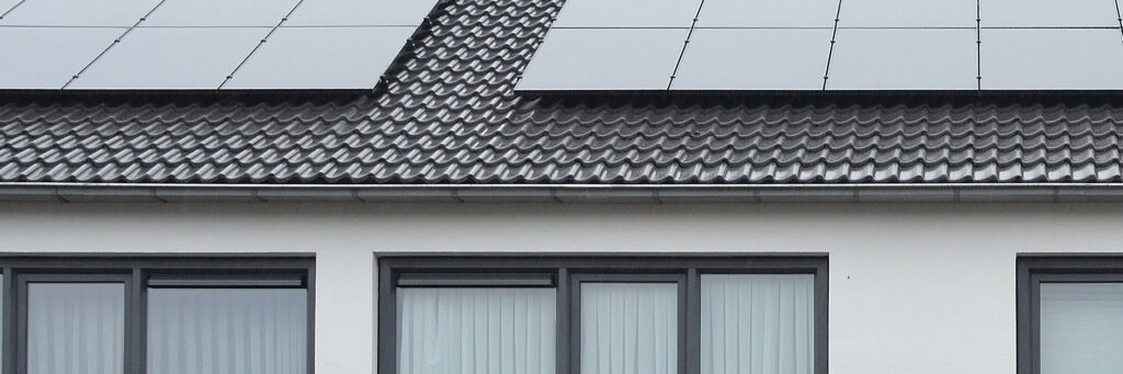 Wit huis met een grijs dak waar pv panelen op liggen