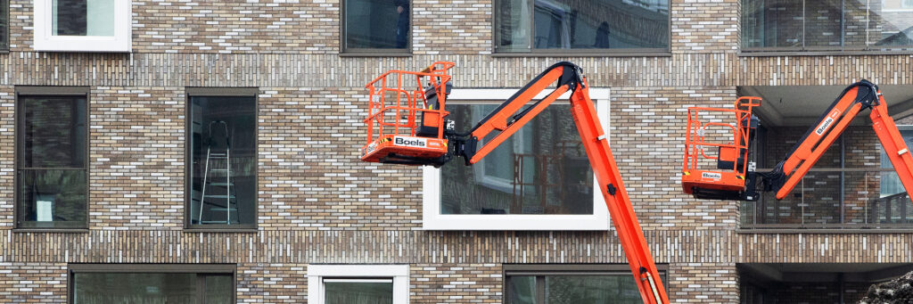 Appartementencomplex met bruine bakstenen gevel met witte kozijnen en twee oranje hoogwerkers voor het complex