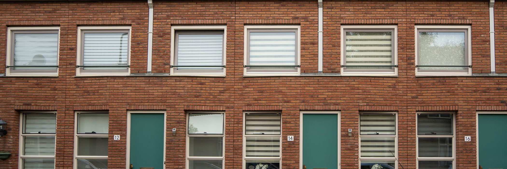 Woningen met bruine bakstenen gevel, witte kozijnen, grijze ramen en groenblauwe deuren