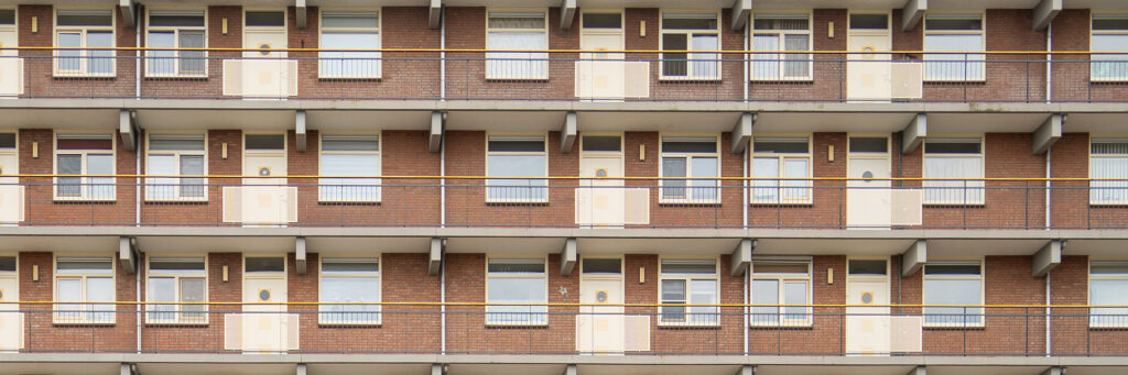 Appartementencomplex met bruine bakstenen gevel, gele kozijnen en deuren en grijs gele balustrade
