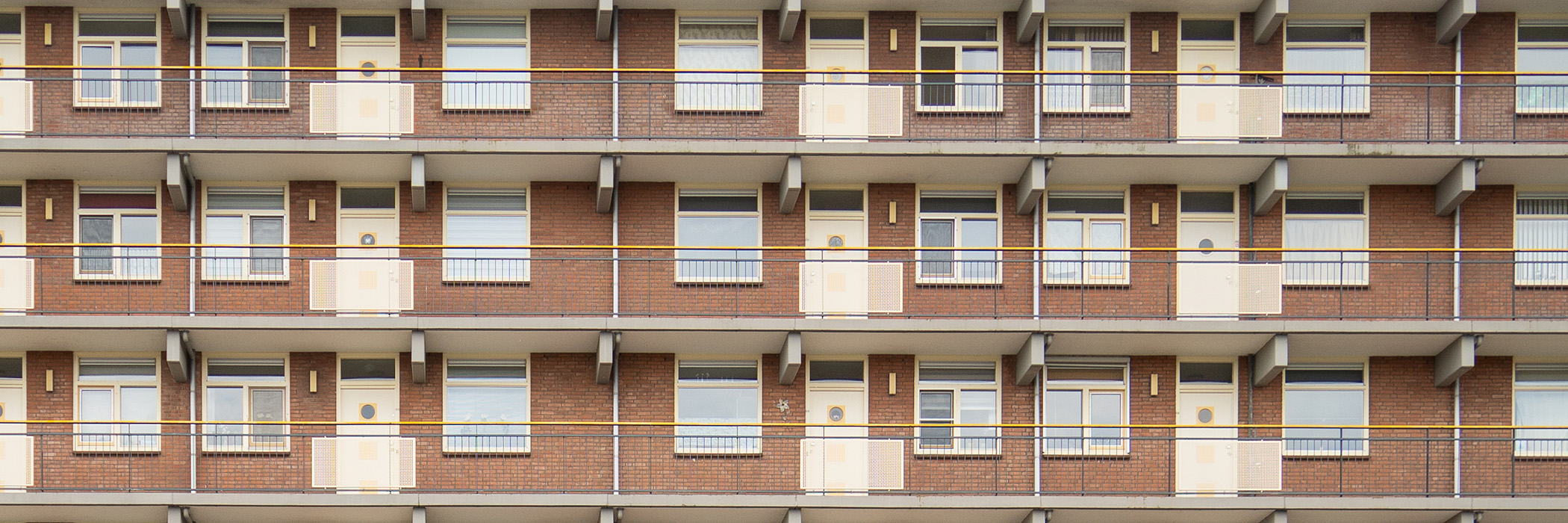 Appartementencomplex met bruine bakstenen gevel, gele kozijnen en deuren en grijs gele balustrade