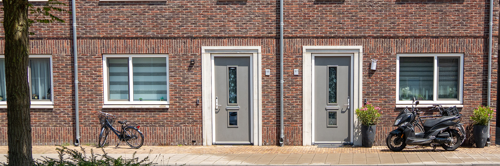 Woningen met bruine bakstenen gevel, witte kozijnen, grijze deuren en scooter en fietsen voor de deur