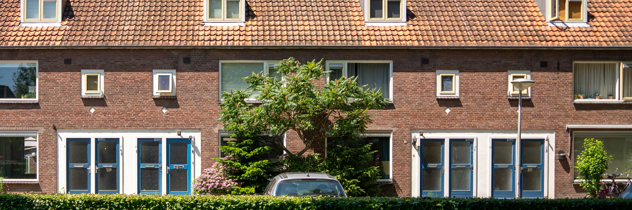 Woningen met bruine bakstenen gevel, rode dakpannen, witte kozijnen en blauwe deuren met een auto ervoor