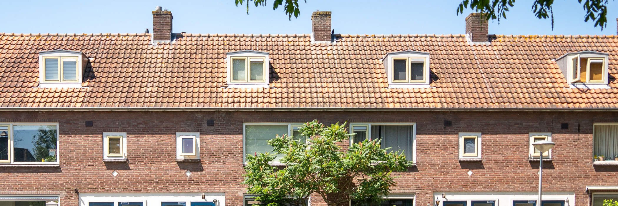Woningen bovenste verdieping met bruine bakstenen gevel, witte kozijnen, gele ramen en een boom voor de deur