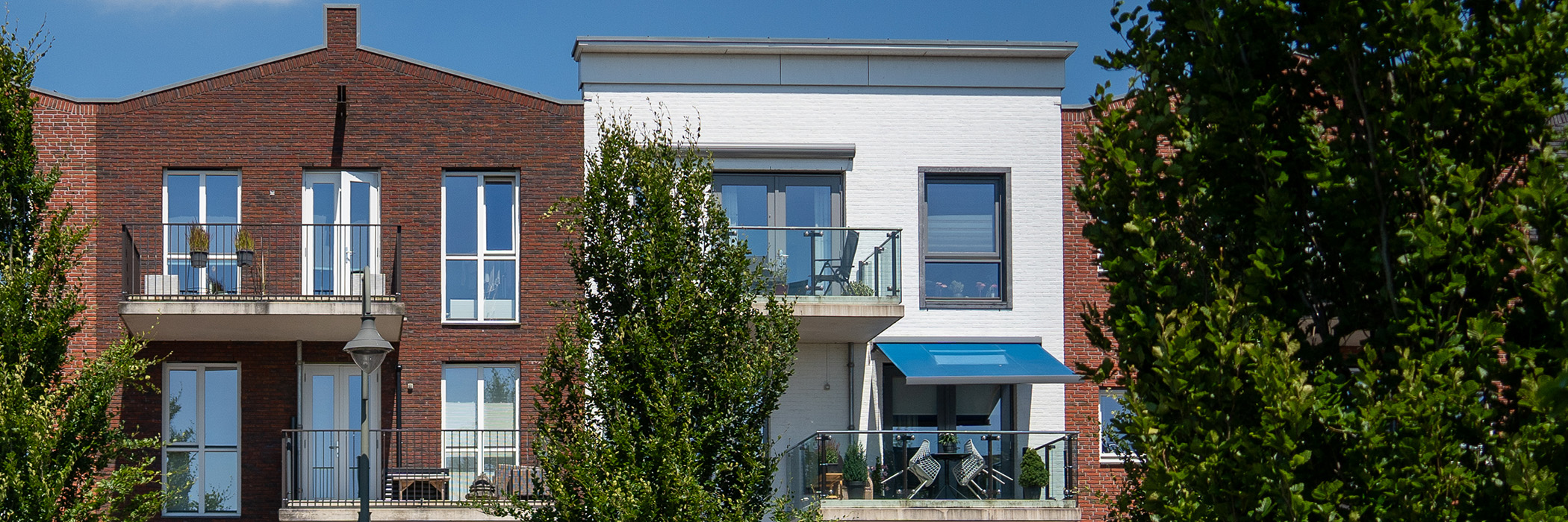 Appartementencomplex met bruine en witte bakstenen gevel, witte en grijze kozijnen met bomen voor de deur