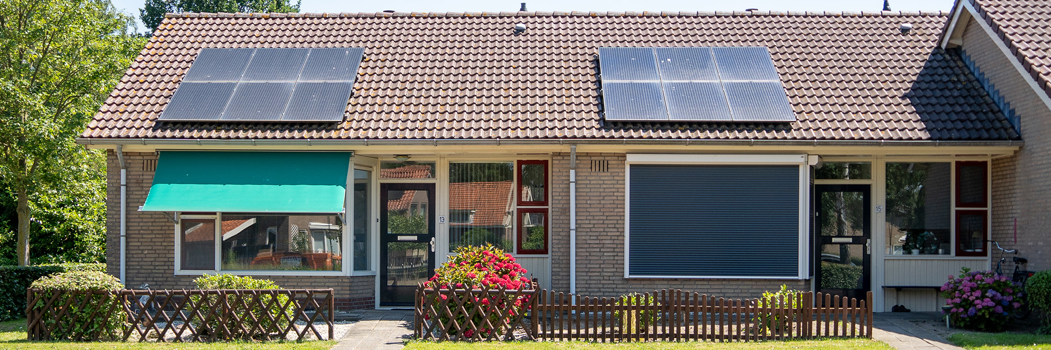 Woningen met bruine bakstenen gevel, witte kozijnen, rode deuren en zonnepanelen op het dak